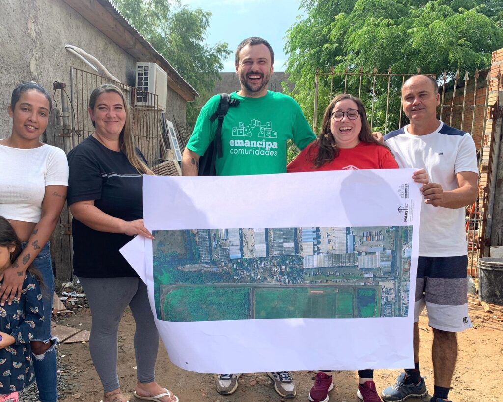 Homens e mulheres no quintal de uma casa segurando nas mãos uma  folha de papel onde está impressa imagem aérea de uma comunidade de Porto Alegre.