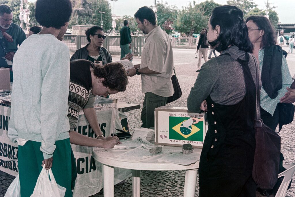 Foto mostrando pessoas numa praça votando no Plebiscito da Dívida Externa, realizado no ano 2000.