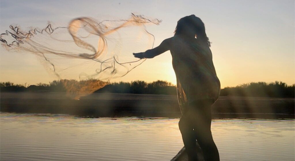 Silhueta de pessoa lançando rede de pesca em barco no pôr do sol.