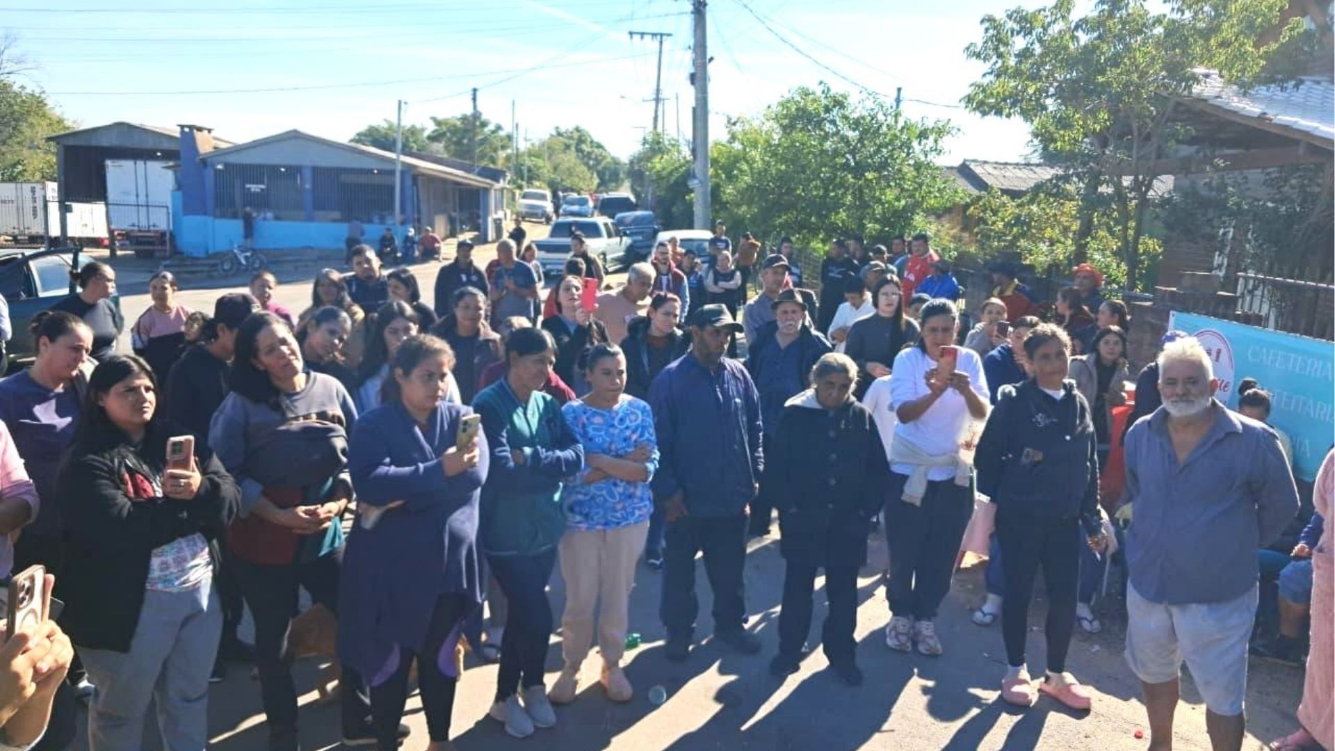 Assembleia comunitária em Vila Dique, grupo engajado com folhetos e celulares durante evento de mobilização popular.