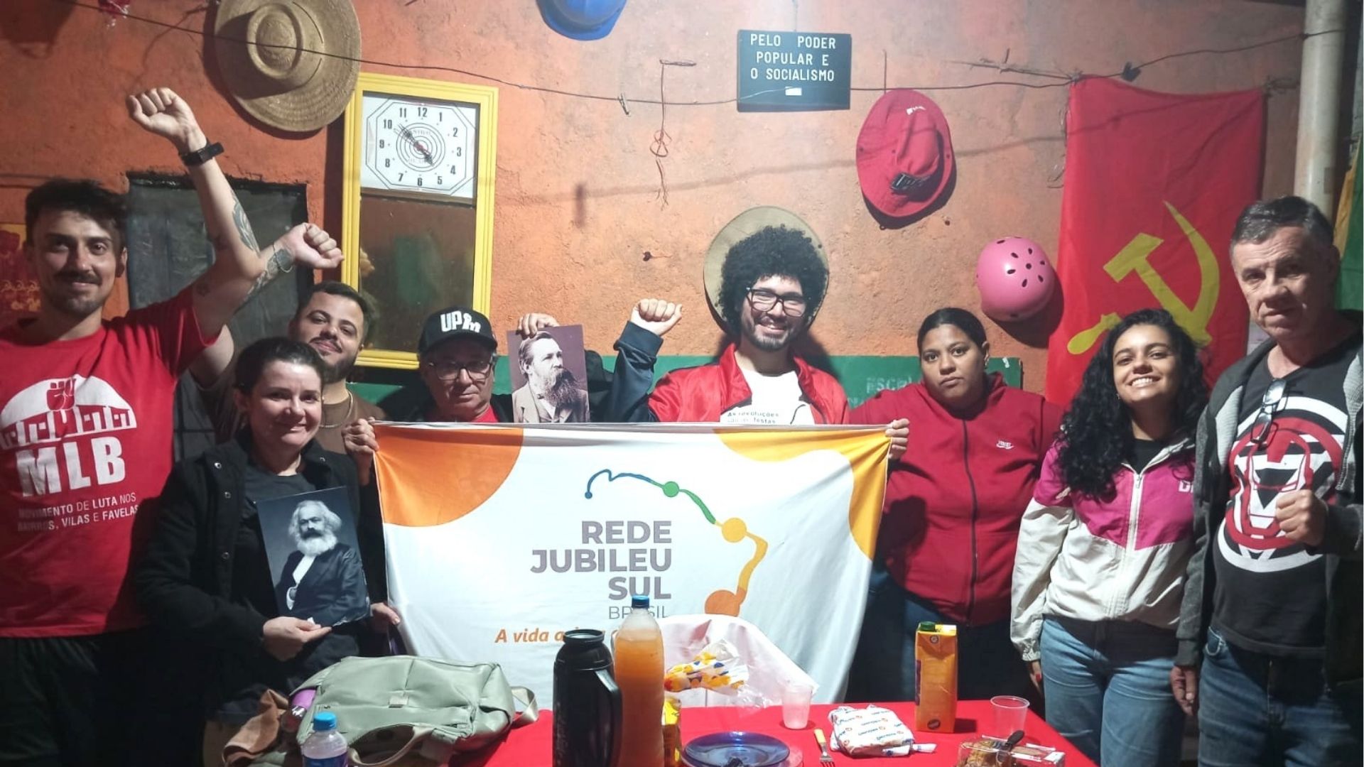 Encontro de cartografia em Jardim Pantanal, grupo segurando faixa "REDE JUBILEU SUL BRASIL - A vida acima de tudo" com painel "PELO PODER POPULAR E O SOCIALISMO" ao fundo, ambiente político engajado.