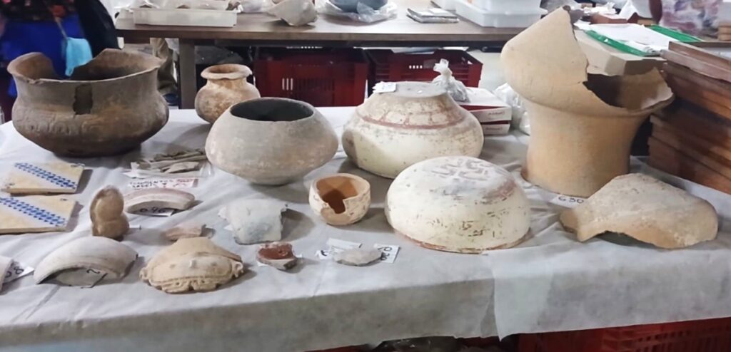 Peças arqueológicas de cerâmica, incluindo potes e fragmentos, expostos em mesa com pano branco durante visita ao Museu da Amazônia, o Musa.