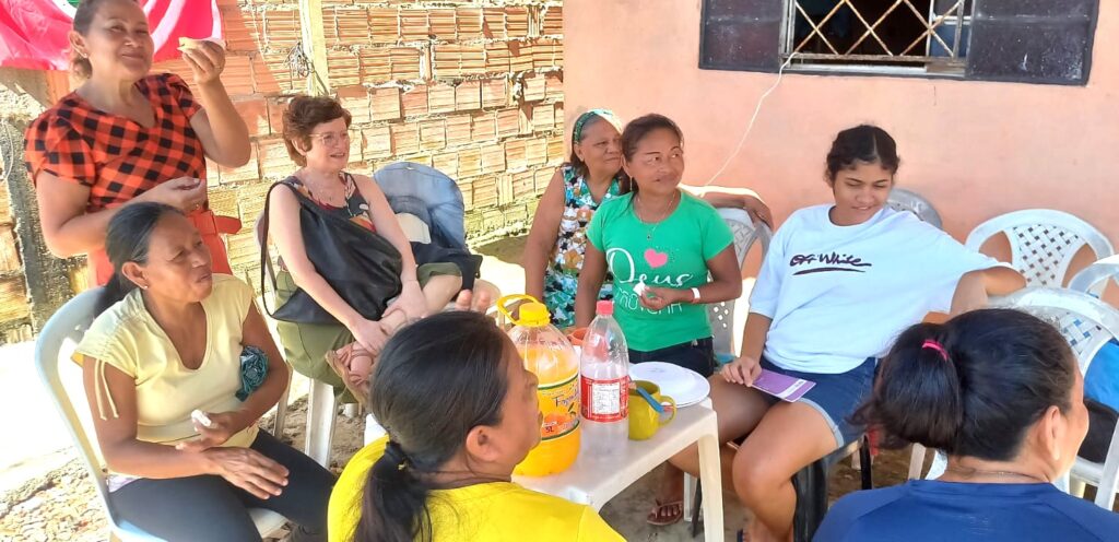 Grupo de mulheres sentadas em círculo ao ar livre, conversando e compartilhando lanche.