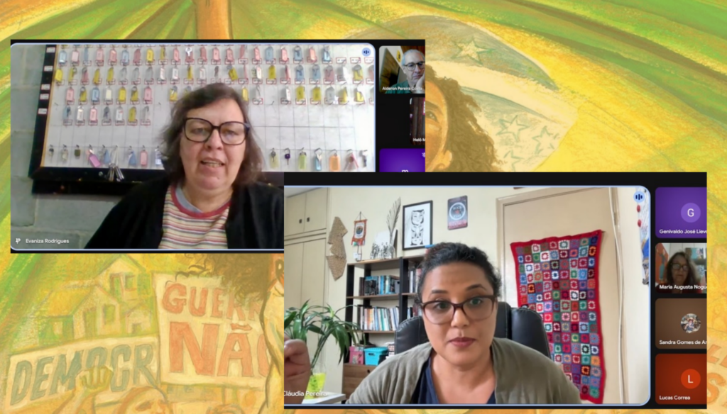 Captura de tela de reunião online com duas participantes principais em destaque. À esquerda, Evaniza Rodrigues fala diante de um quadro com etiquetas coloridas. Abaixo, Cláudia Pereira aparece em seu ambiente doméstico com estante de livros e tapeçaria artesanal ao fundo. Fundo da tela exibe arte gráfica amarela com frases políticas como "DEMOCRACIA" e "GUERRA NÃO".